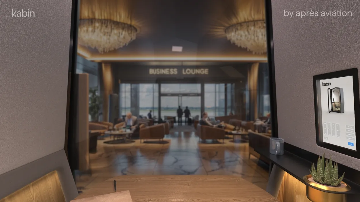 First-person POV from inside Kabin by Après Aviation, showing the private desk layout and a clear view facing out toward a busy airport business lounge.